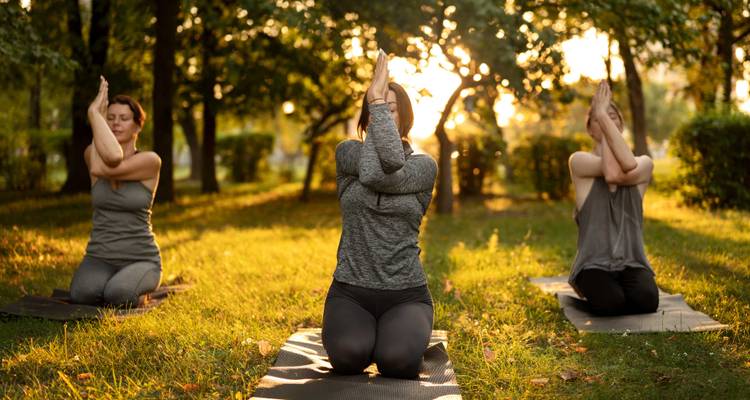 Drie mensen die yoga beoefenen op matjes in een park tijdens zonsondergang.