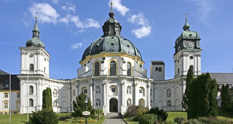 Barocke Abtei Ettal mit Zwillingstürmen und grüner Kupferkuppel unter blauem Himmel in Bayern.
