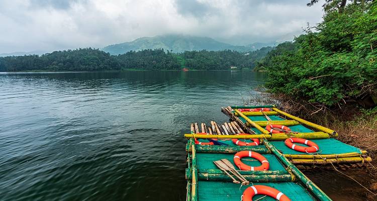 Bamboo rafts floating on a calm lake with wooded hills in the background.
