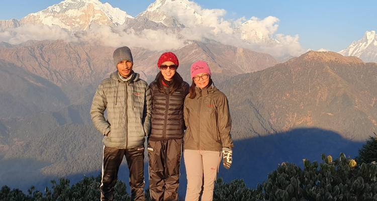 Drie wandelaars in jassen staan voor het zonnige Annapurna gebergte en blauwe hemel