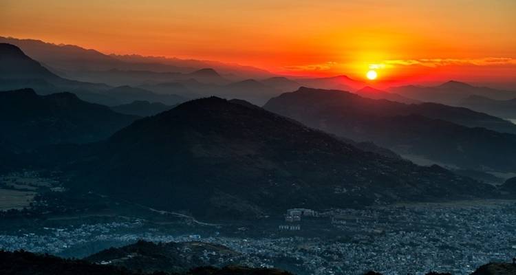 Levendige zonsopgang werpt oranje gloed over gelaagde bergkammen boven de vallei van Pokhara