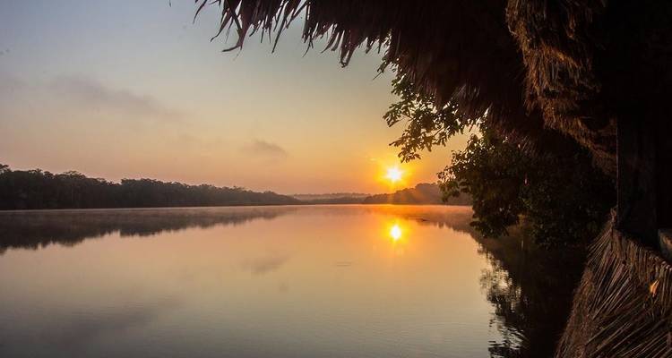 Tranquila escena fluvial con la salida del sol y una cabaña con tejado de paja.