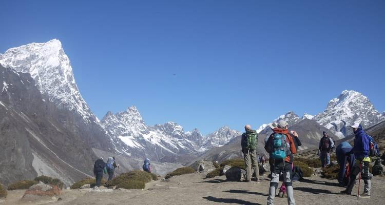 Wandelgroep trekt langs een bergtrail op grote hoogte met scherpe, sneeuwbedekte toppen op een heldere dag.