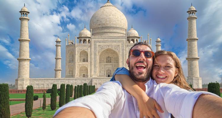 Selfie de una pareja feliz frente al Taj Mahal bajo un cielo azul brillante.