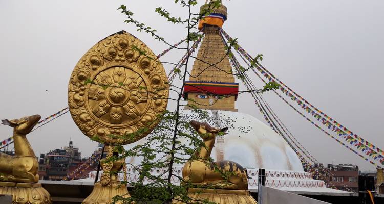 Golden deer and Dharma wheel statue framing Boudhanath Stupa in the background