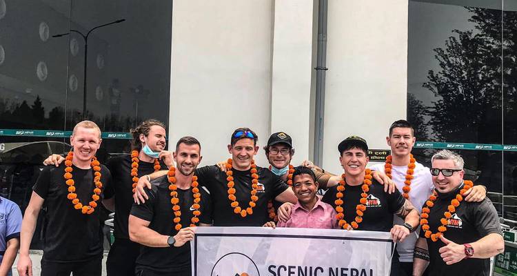 Groupe de trekkeurs portant des guirlandes de souci posant avec une bannière Scenic Nepal à l'arrivée.