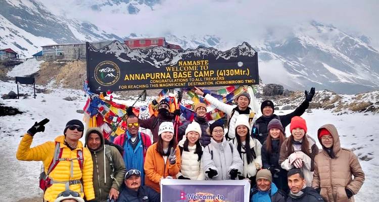 Grote, vrolijke trekkinggroep viert feest in de verse sneeuw bij het Annapurna Base Camp-bord.