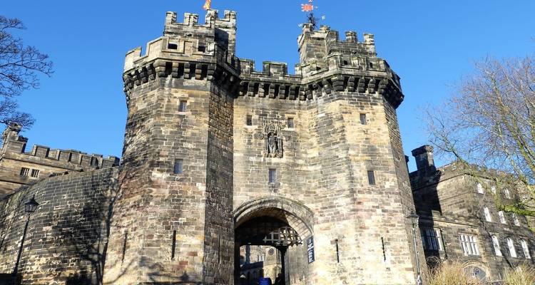 Impresionante puerta de piedra con almenas de un castillo medieval que se alza contra un cielo azul despejado.