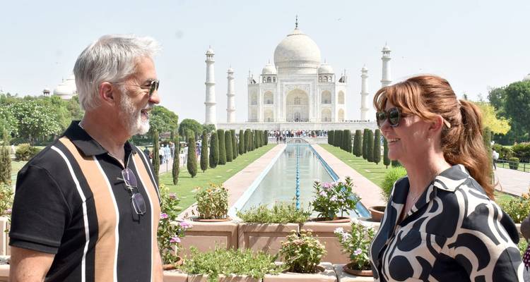 Pareja sonriente posa frente al estanque reflectante que conduce al Taj Mahal.