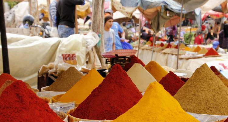 Pirámides vibrantes de especias rojas, amarillas y marrones en venta en un mercado bullicioso.