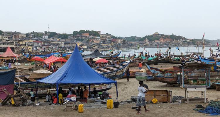 Escena bulliciosa de mercado con barcos y carpas coloridas cerca del agua.