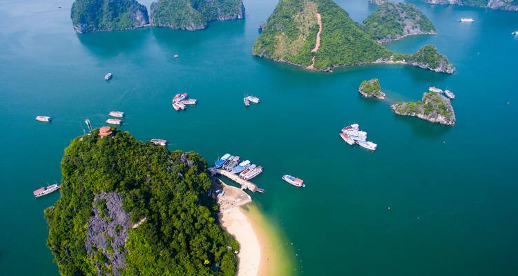 Vista aérea de islas color esmeralda y barcos dispersos en las aguas azul profundo de la Bahía de Ha Long.