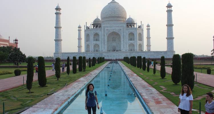 Een zicht op de Taj Mahal met bezoekers die rond de spiegelende vijver wandelen.