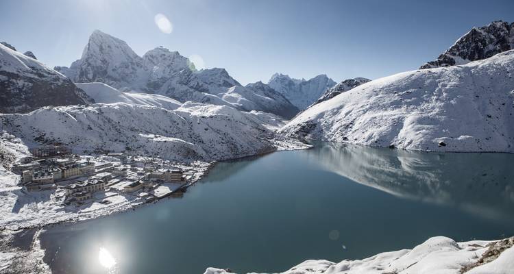 Montagnes enneigées avec un lac réfléchissant, petit village au bord du rivage.