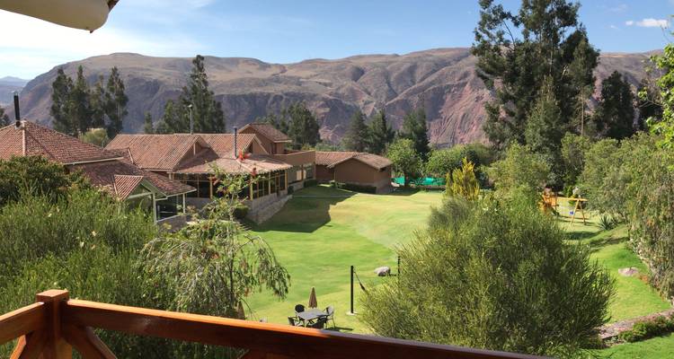 Blick auf einen gut angelegten Garten mit Gebäuden und Bäumen vor einer Bergkulisse.