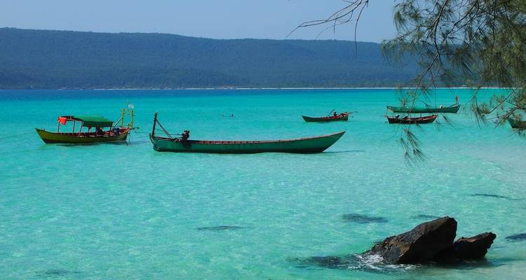 Kleine Boote treiben auf dem klaren türkisfarbenen Wasser mit einer bewaldeten Insel im Hintergrund.