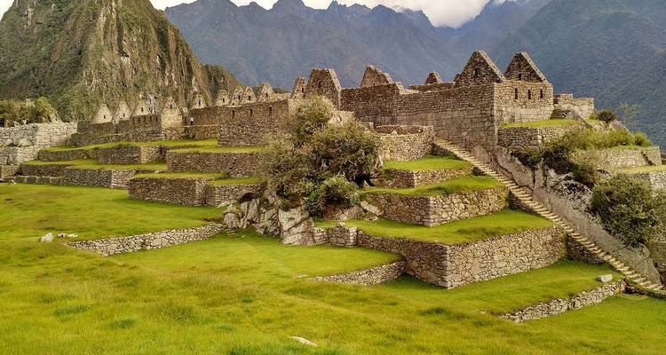 Terrasses de pierre et anciennes ruines incas encadrées par une herbe verte luxuriante et des montagnes brumeuses au Machu Picchu