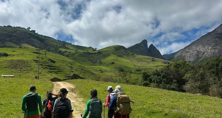 Excursionistas vestidos con equipo de montaña caminando por un sendero cubierto de hierba en una zona montañosa.