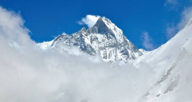 Eine scharfe Spitze eines schneebedeckten Berges inmitten von Wolken.