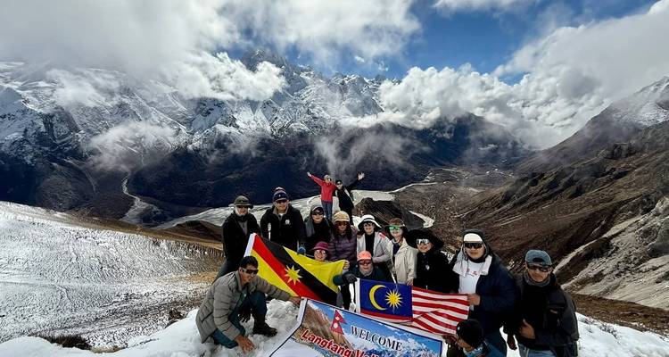 Un grand groupe de trekking posant avec les drapeaux malaisien et sarawakien sur une crête enneigée dans l'Himalaya.