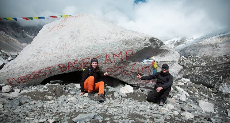Two trekkers kneel beside the famous Everest Base Camp boulder marked 5364 m.