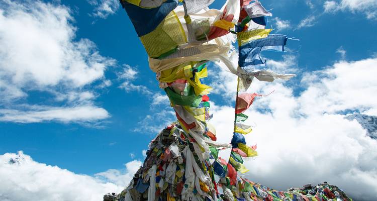 Colorful prayer flags flutter against a bright blue sky in the Himalayas.