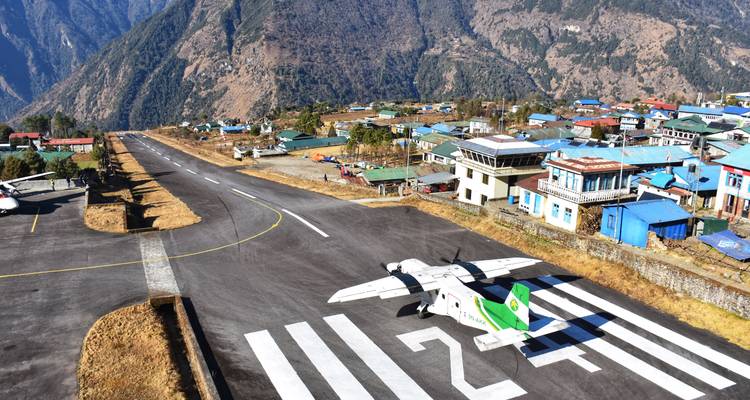 Pequeño avión en la pista inclinada del Aeropuerto de Lukla con las estribaciones del Himalaya y edificios del pueblo cerca.
