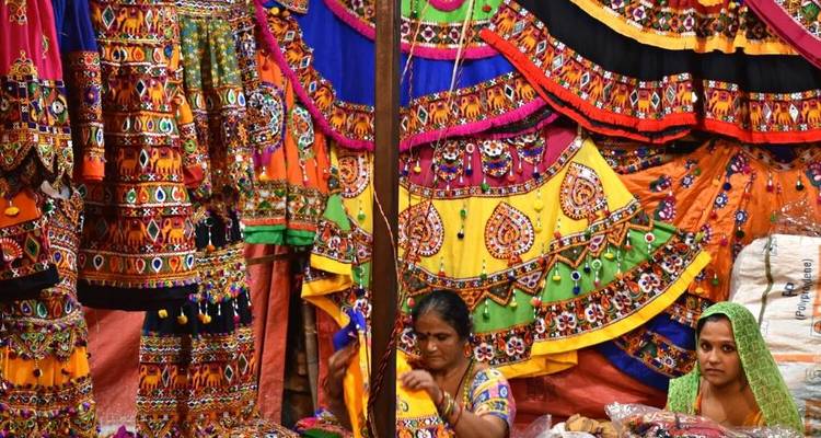 Vêtements traditionnels colorés exposés dans un marché avec des gens qui fabriquent.