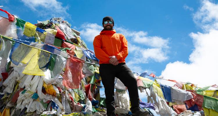 Persona de pie frente a banderas de oración coloridas en un paso de montaña.
