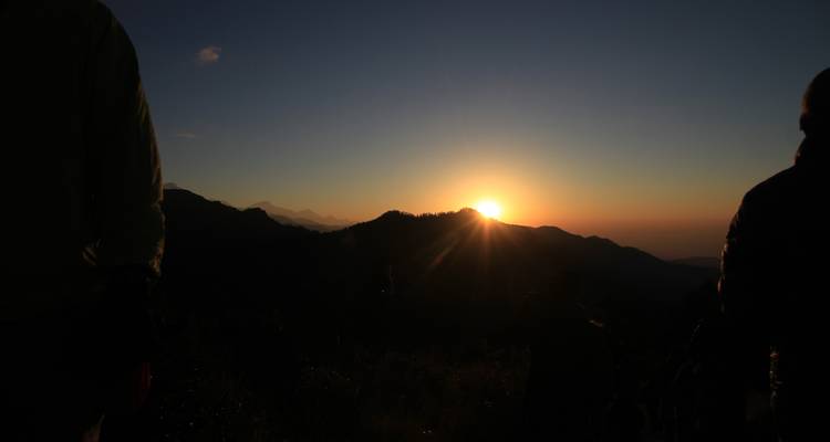 Silhouette of people watching a sunrise over mountains.
