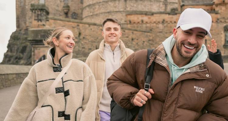 Des amis souriants se promenant à l'extérieur d'un château de pierre historique en Écosse