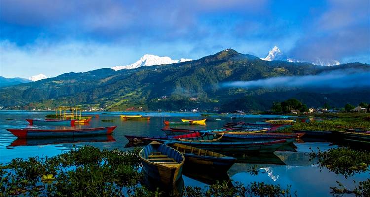 Bateaux colorés sur un lac serein avec des montagnes en arrière-plan sous un ciel dégagé.