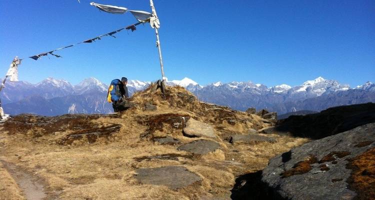 A hiker with a backpack and prayer flags on a rocky mountain peak.