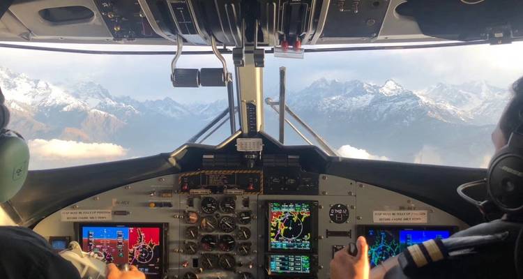 Blick aus dem Cockpit eines Flugzeugs, das über bergiges Gelände fliegt.