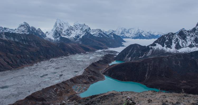 Eine dramatische Landschaftsansicht von schneebedeckten Bergen und einem türkisfarbenen Gletschersee.