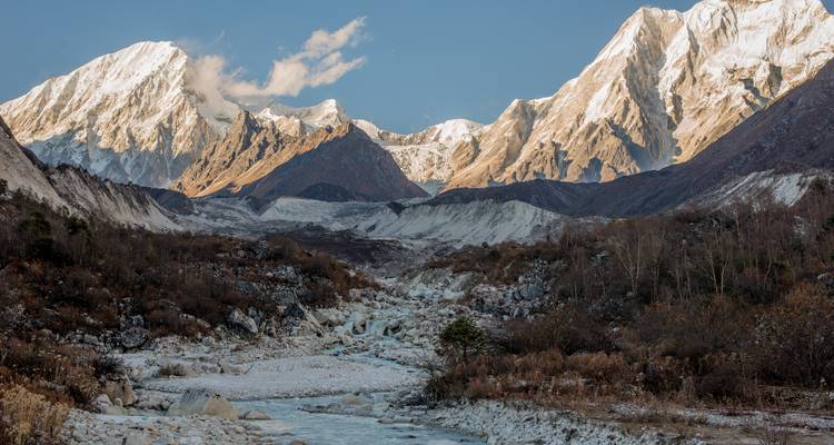 Snow-covered mountains with a rocky valley and river in the foreground.