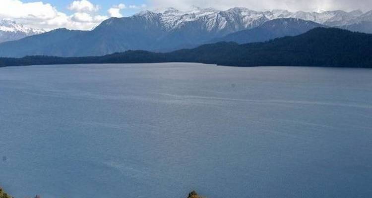 See mit entfernten schneebedeckten Bergen unter einem bewölkten Himmel.