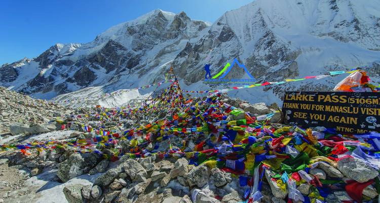 Gebedsvlaggen en een bord bij een bergpas met besneeuwde toppen.