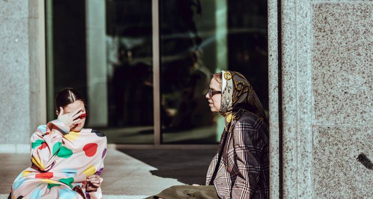 Two women sitting outside a building with reflective glass.