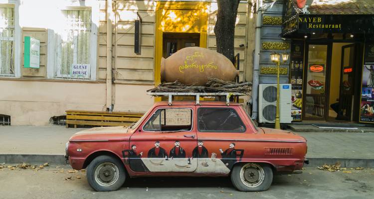 Retro car parked on a street with a pig sculpture on its roof.