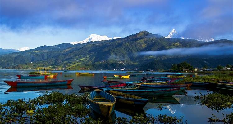 Bateaux colorés sur un lac avec des montagnes enneigées en arrière-plan.