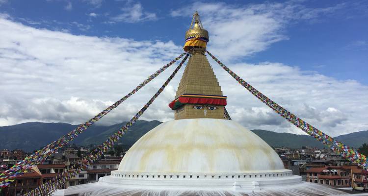 Eine große Stupa mit bunten Gebetsfahnen vor einem wolkenverhangenen Himmel, typisch für Kathmandu.