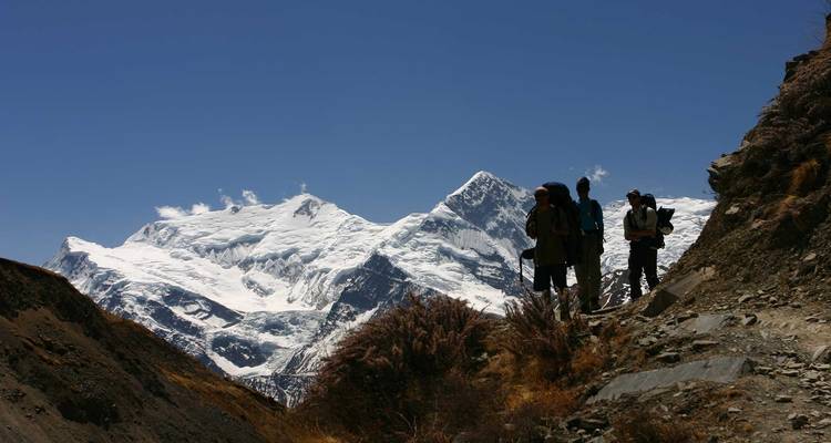 Hikers on a trail with snowy mountains in the backdrop.