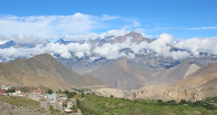 Panoramic view of a mountainous region with clouds and a village on the hillside.