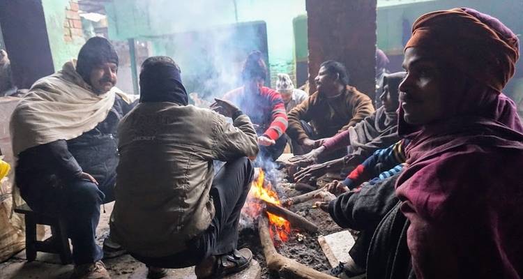 Eine Gruppe von Menschen versammelt sich um ein kleines Feuer in einem Haus.