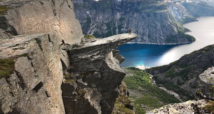 Aventurier se tenant sur la spectaculaire falaise de Trolltunga surplombant un fjord d'un bleu profond.