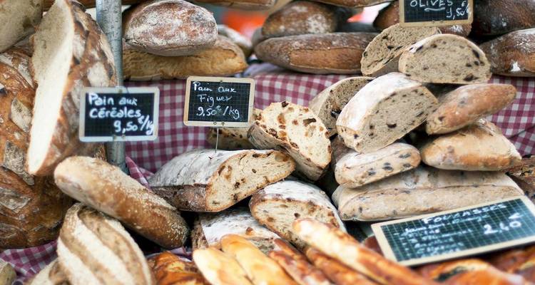Montones de panes franceses artesanales y baguettes exhibidos en un puesto de mercado con pequeños letreros de pizarra.