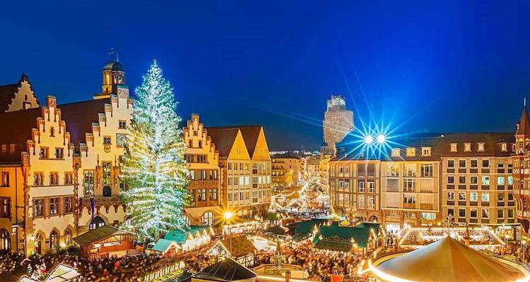 Un animado mercado navideño y edificios iluminados crean una escena nocturna festiva de la ciudad.