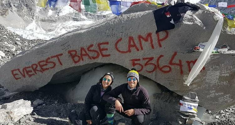 Deux trekkeurs posent au rocher du camp de base de l'Everest entouré de drapeaux de prière et de glace.