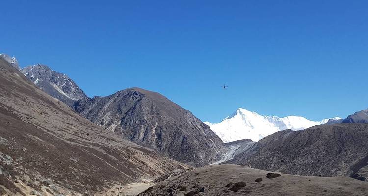 Paisaje de alta montaña con un pequeño helicóptero en el cielo.